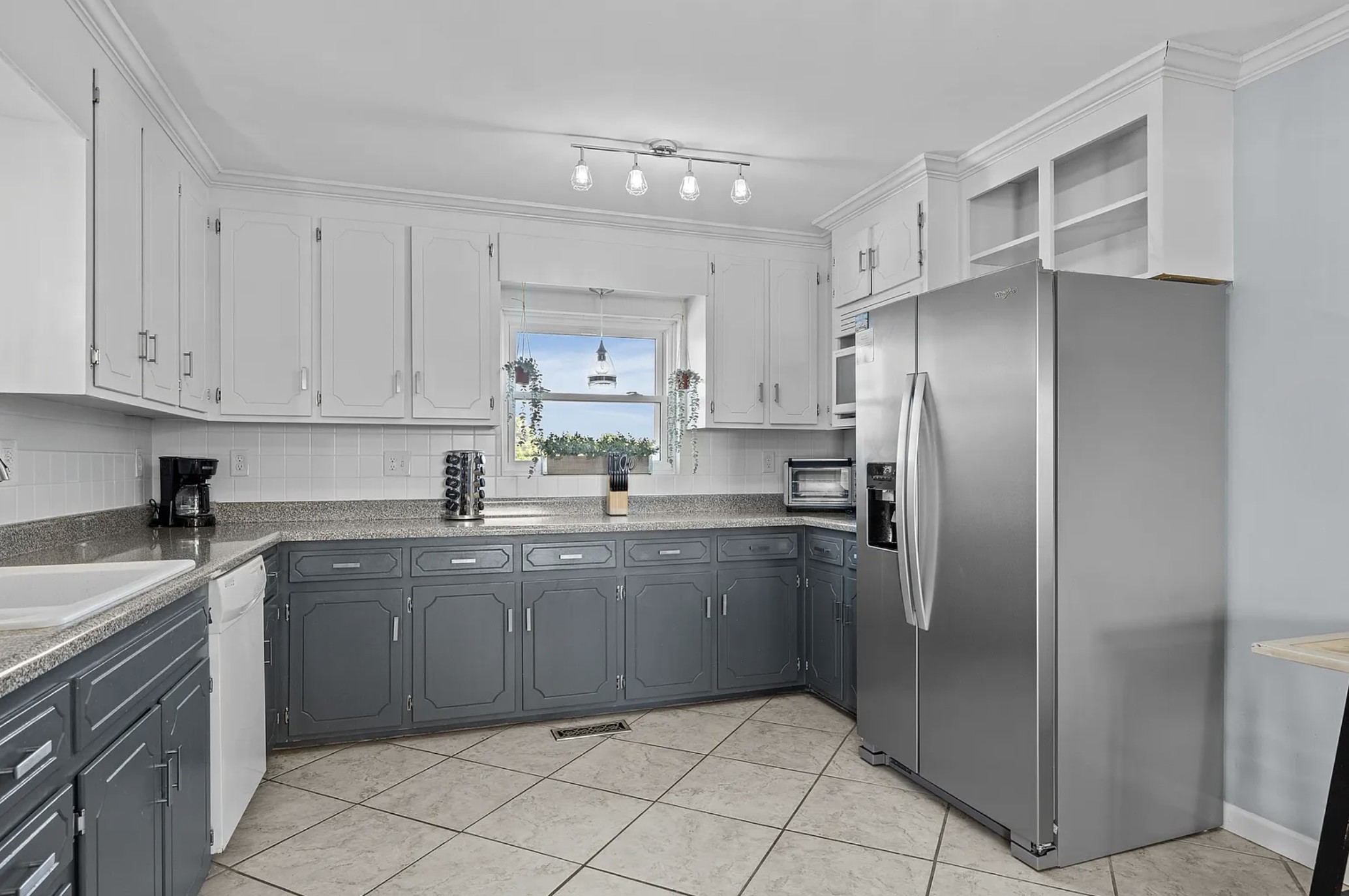 Kitchen with white upper cabinets, gray lower cabinets, and stainless refrigerator